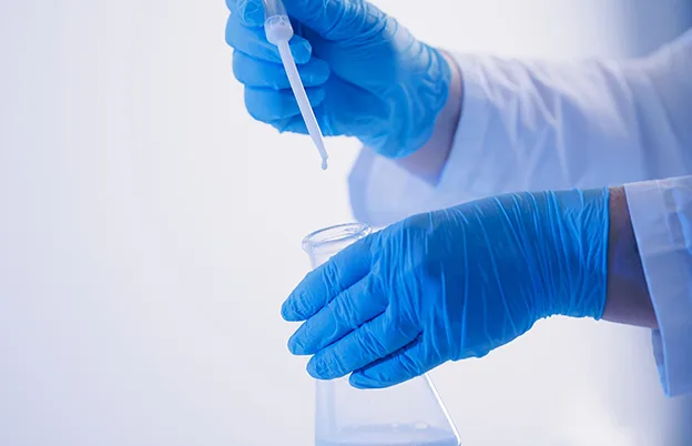 scientist with gloves using dropper and beaker